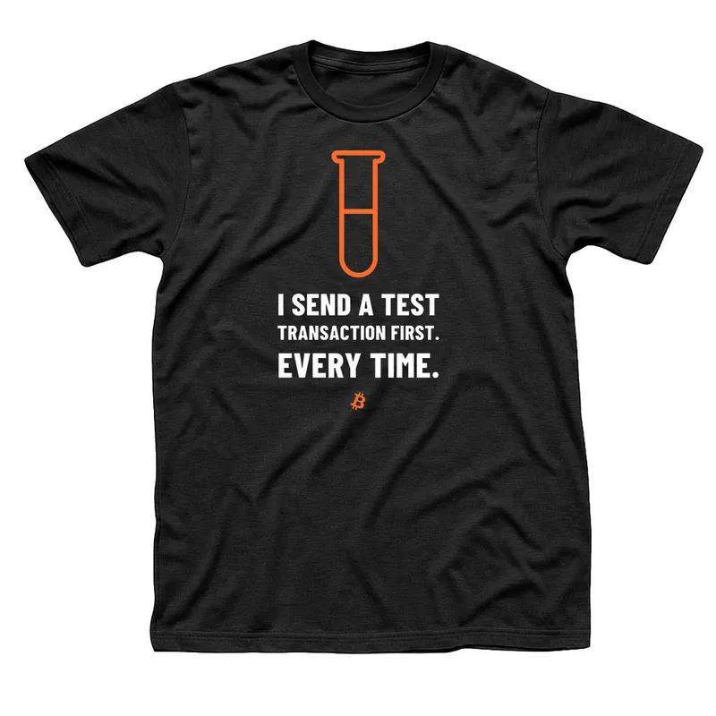 Black t-shirt with an orange test tube above I Send a Test Transaction First, Every Time in white capitals and a small orange Bitcoin symbol below